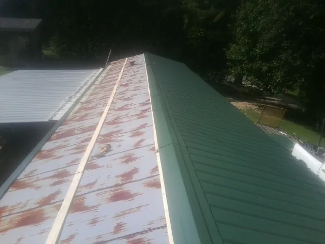 Old rusted panels beside newly installed green metal roofing — Wind Damage Roof Repair by Roofing Brothers in Central
