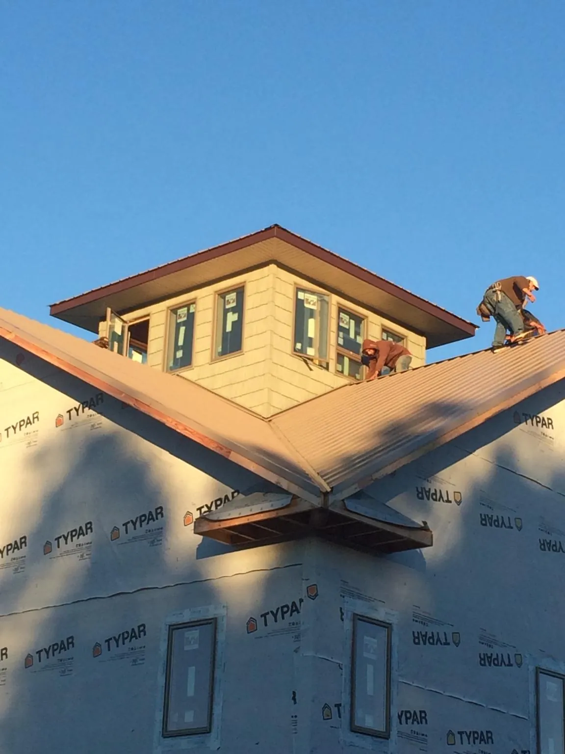 Roofers working around a rooftop cupola on a new metal roof at sunset — Roof Waterproofing in Central by Roofing Brothers